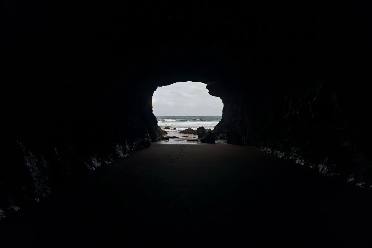 Looking out of a dark sea cave towards a bright beach and breaking waves