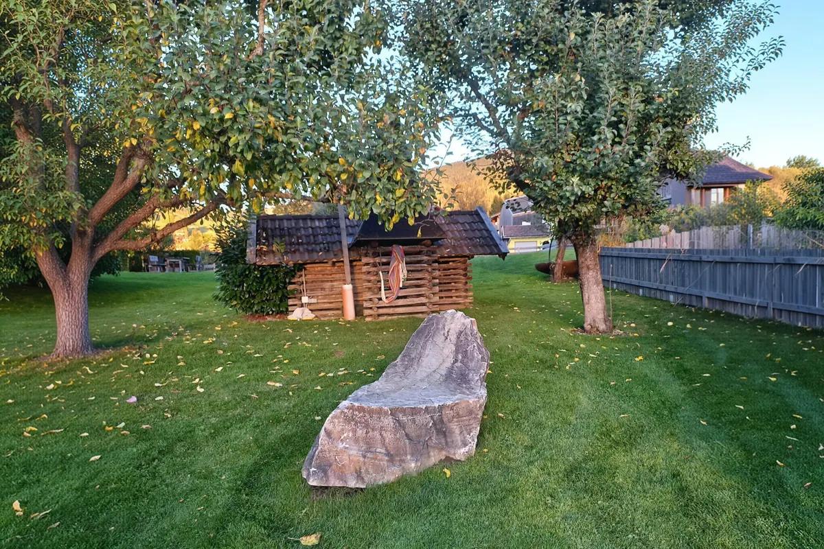 A green garden with mature fruit trees, grass and a broad natural stone seat