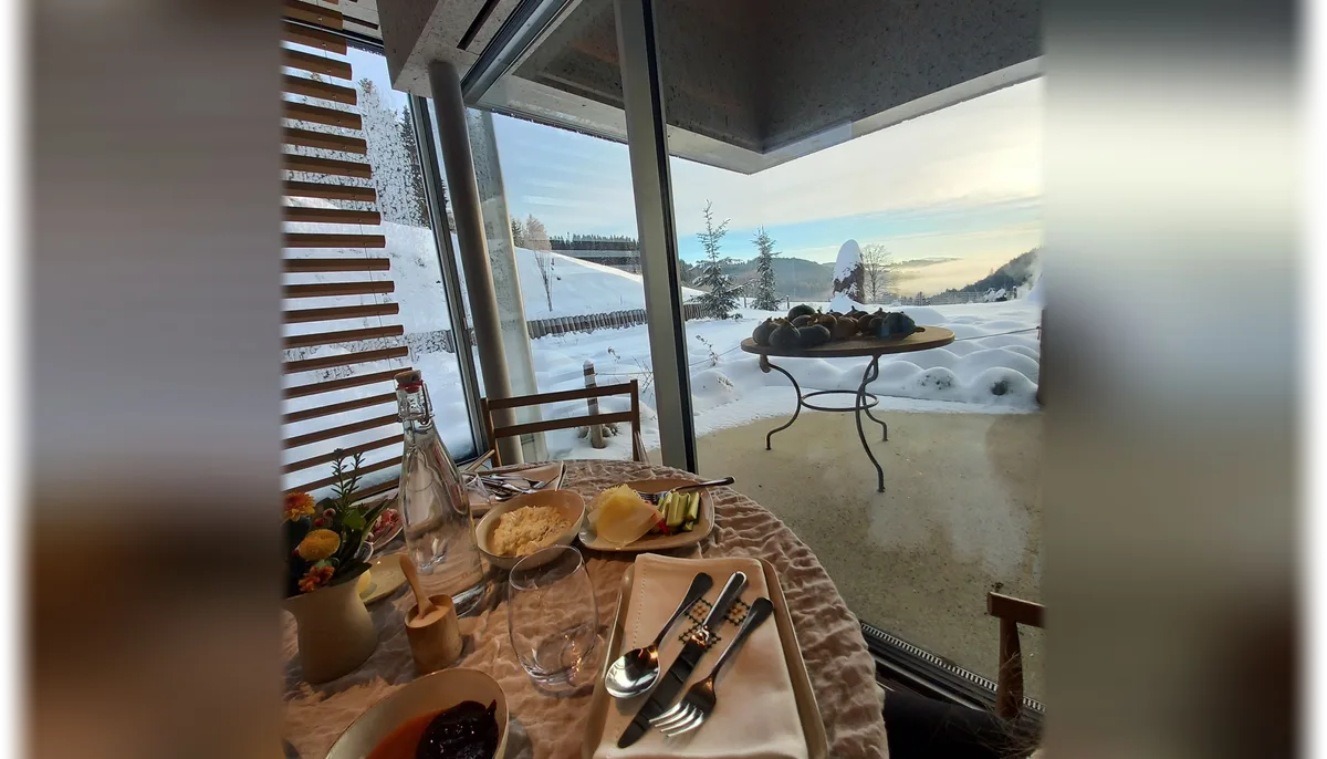 A breakfast table laid by a wide window looking out over deep snow and pine forest at first light