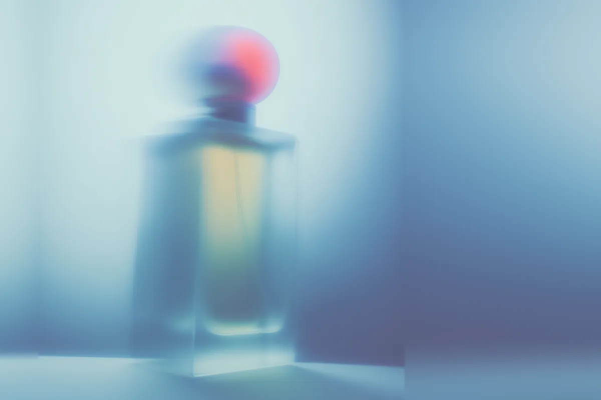 A perfume bottle seen through frosted glass, softened into blue and coral light