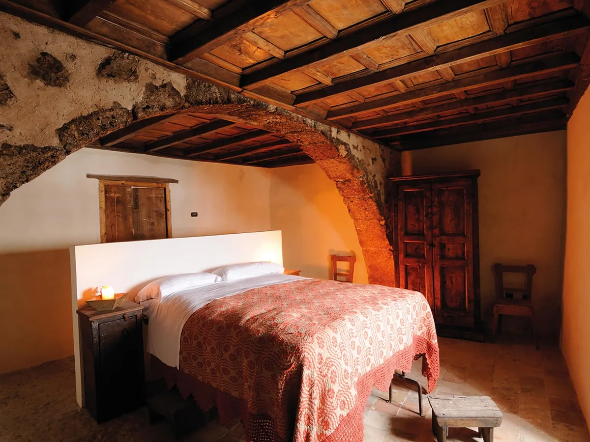 A Sextantio bedroom with old stone, timber, wooden furniture and a woven bedcover