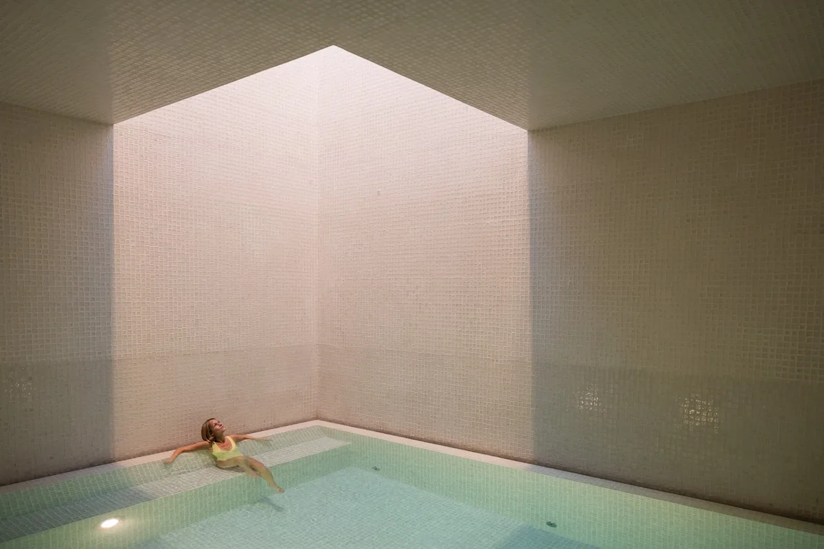 A guest resting in the softly lit indoor pool at Waldhaus Sils