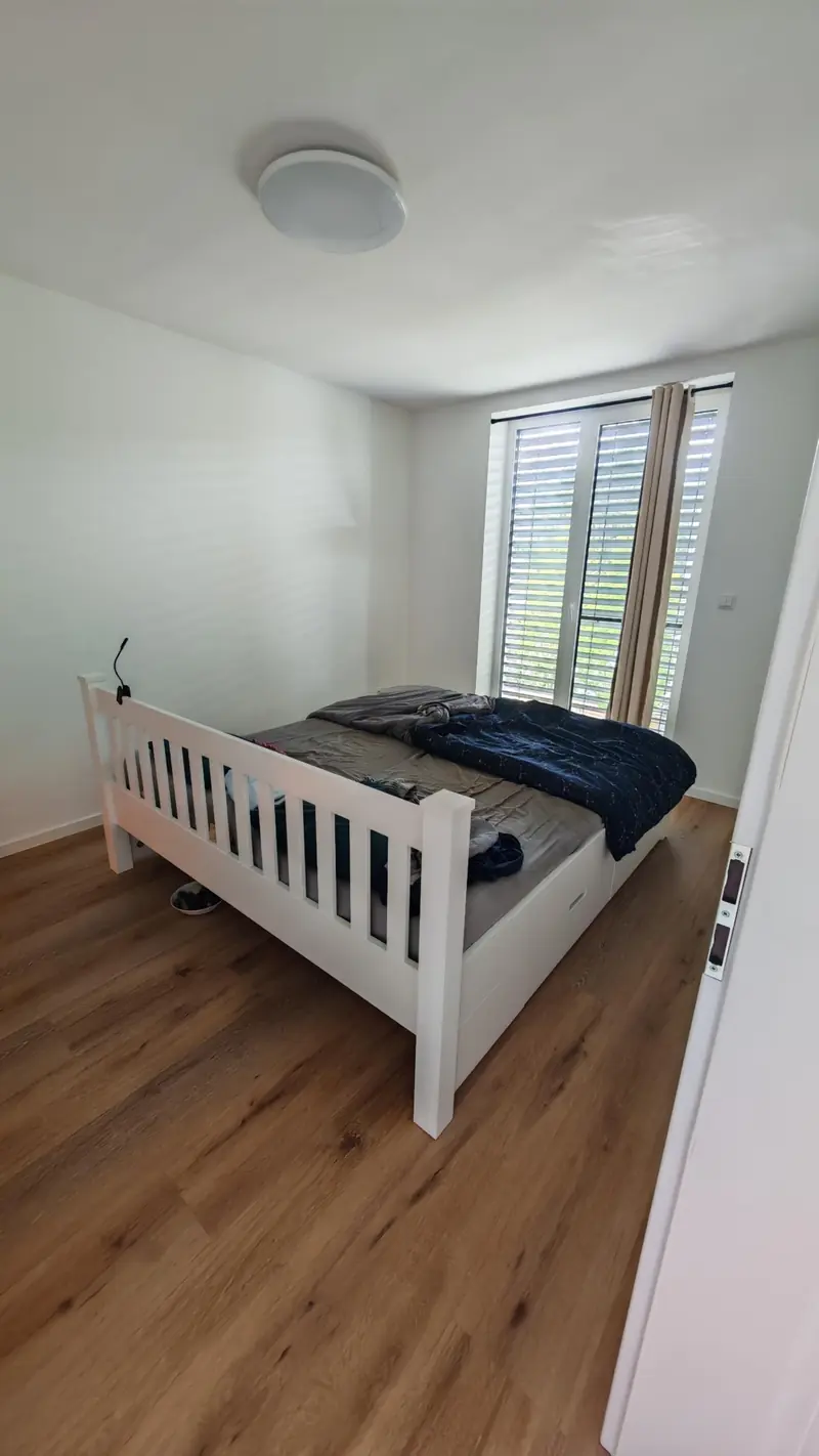 A bed standing free of the walls, shutters at the glass